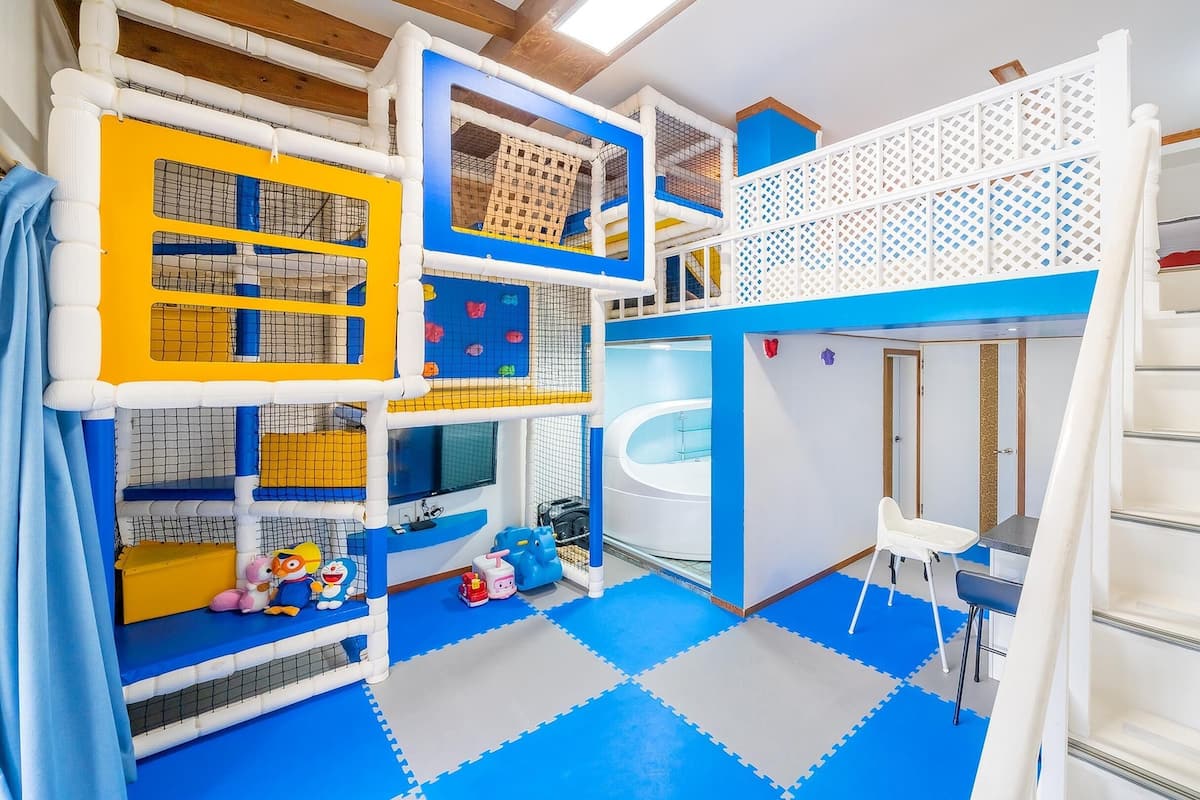 A multi-level play area with various climbing structures and a slide, surrounded by padded flooring and a white railing.