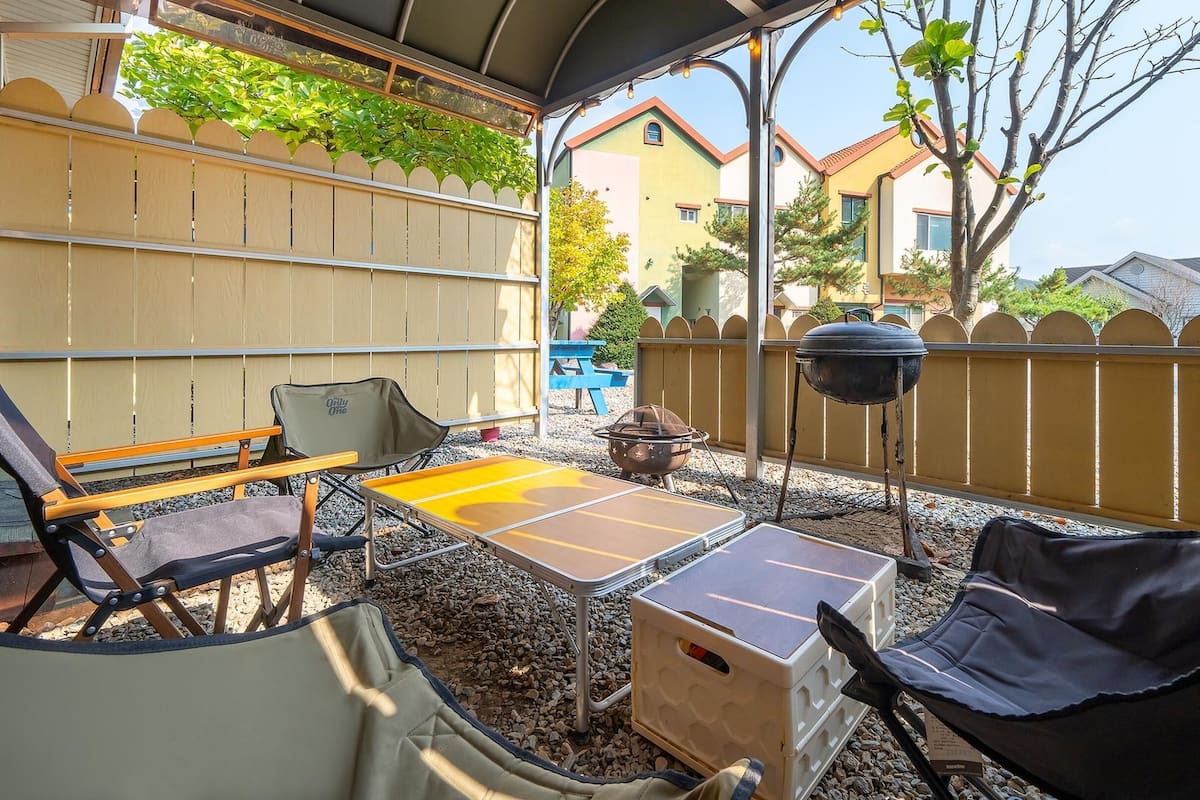 A covered outdoor patio with seating, a grill, and a view of a residential area.