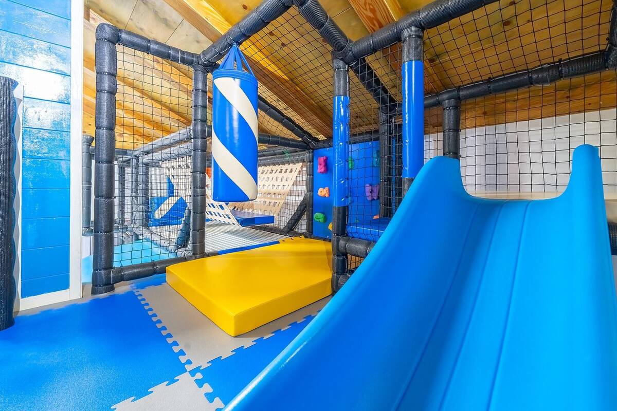 An indoor play area with a blue slide, climbing walls, and padded flooring.