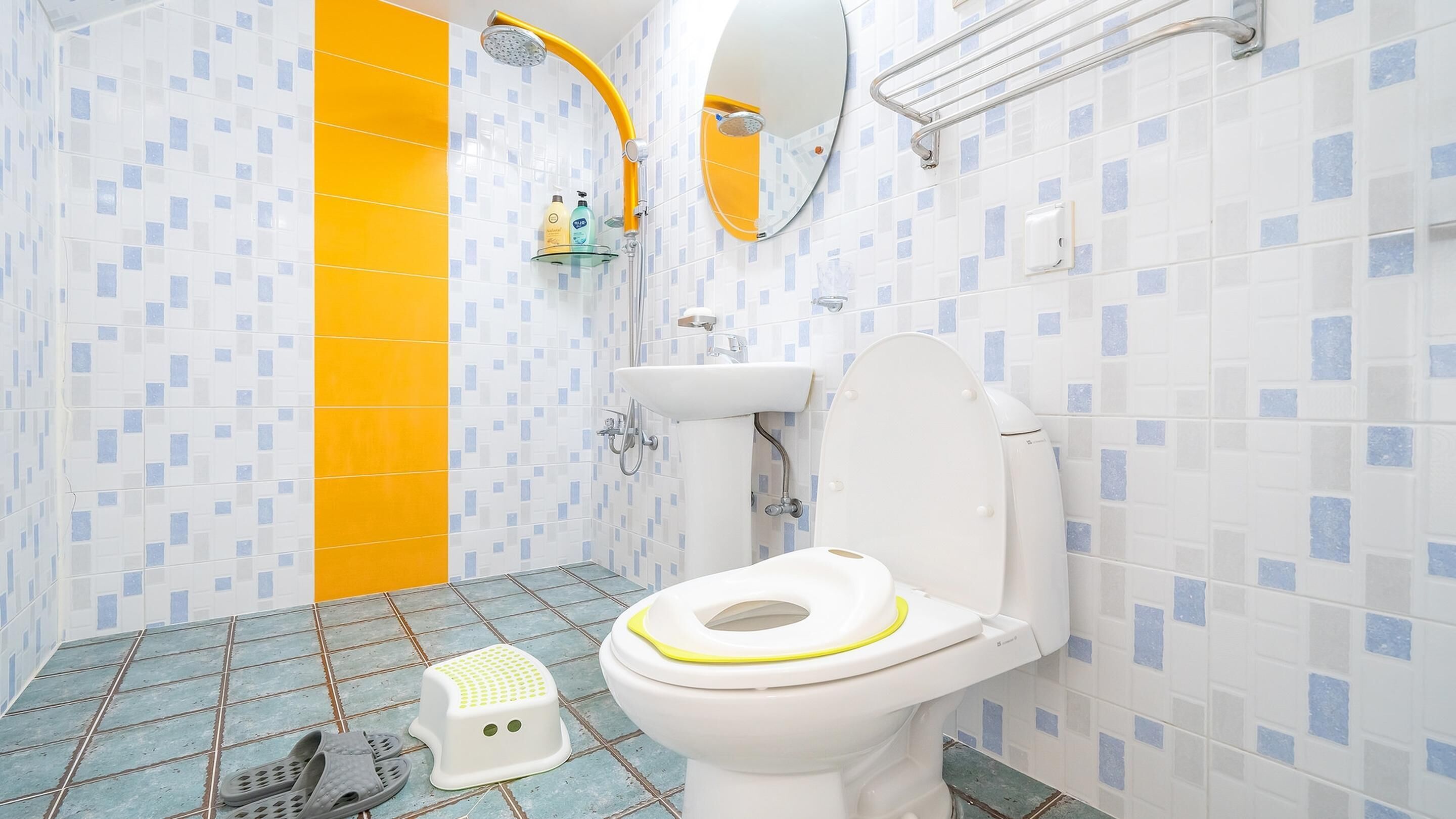 Un baño con inodoro blanco, zona de ducha con azulejos amarillos y un lavamanos.