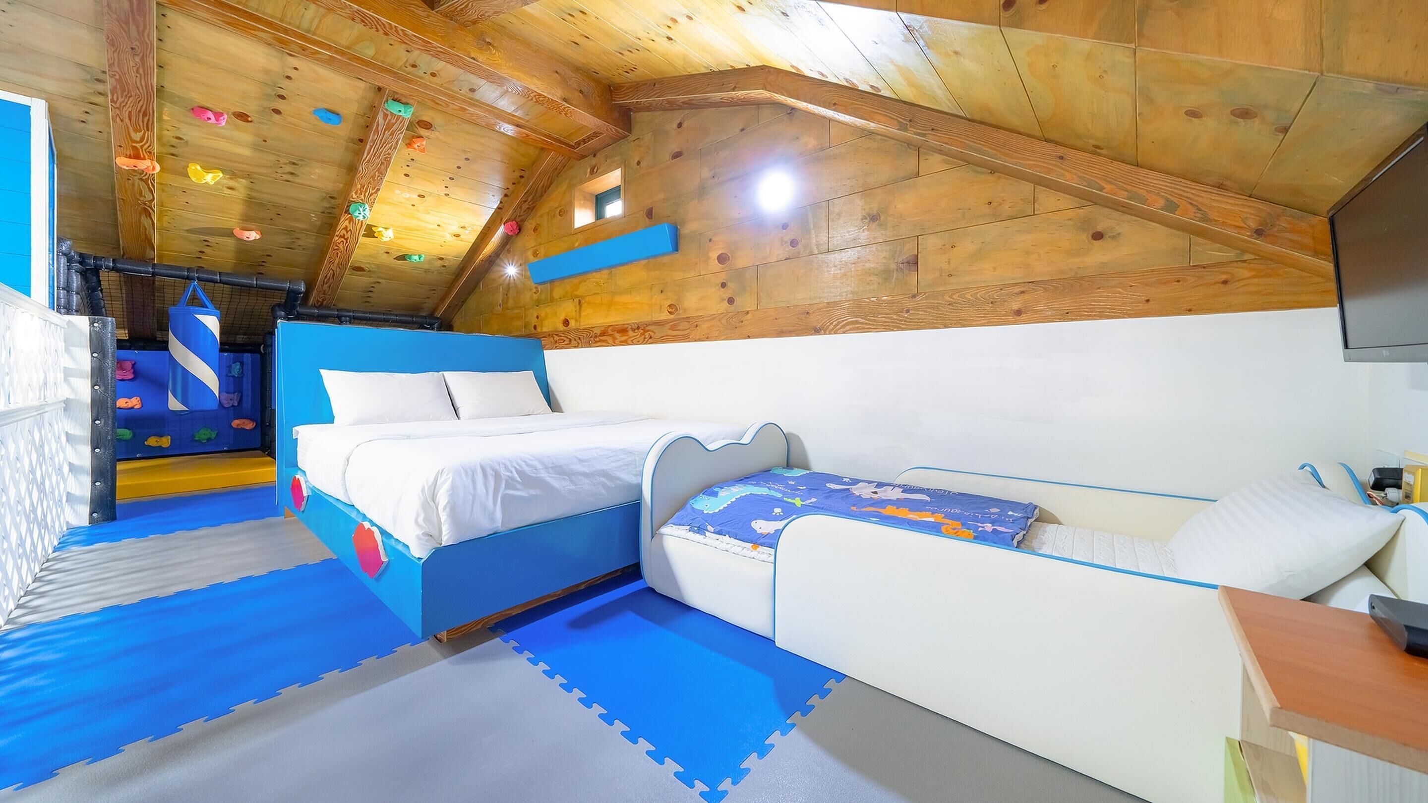 Ein Zimmer mit Etagenbett und Schlafsofa, Holzboden, Kletterwand und Fernseher.