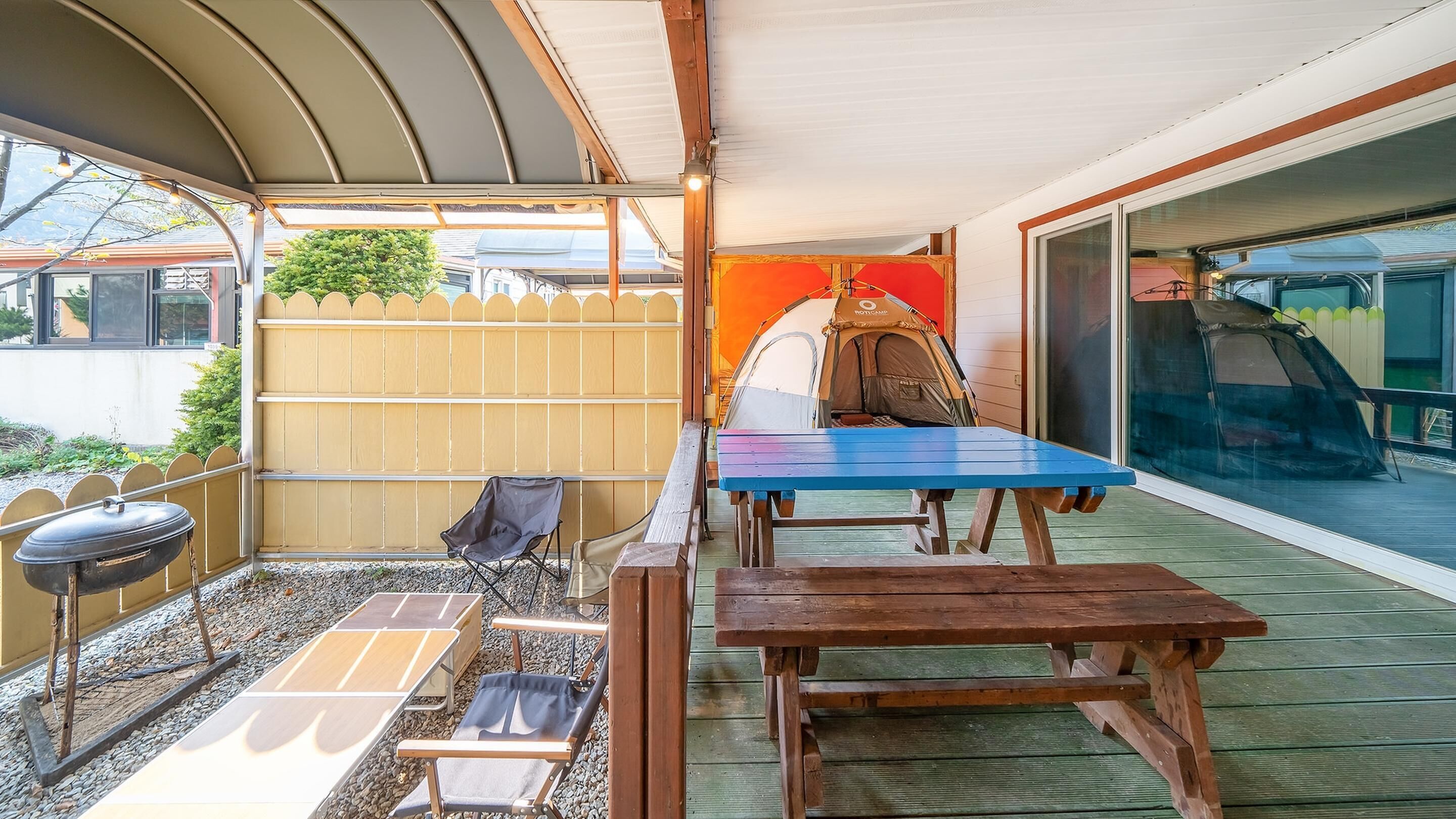 A covered patio with a wooden table and chairs, a grill, and a tent.