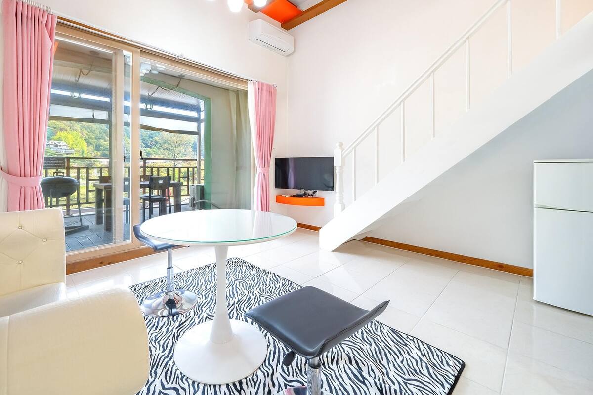 A modern living room with a glass table, a sofa, a zebra-patterned rug, and a TV on the wall.