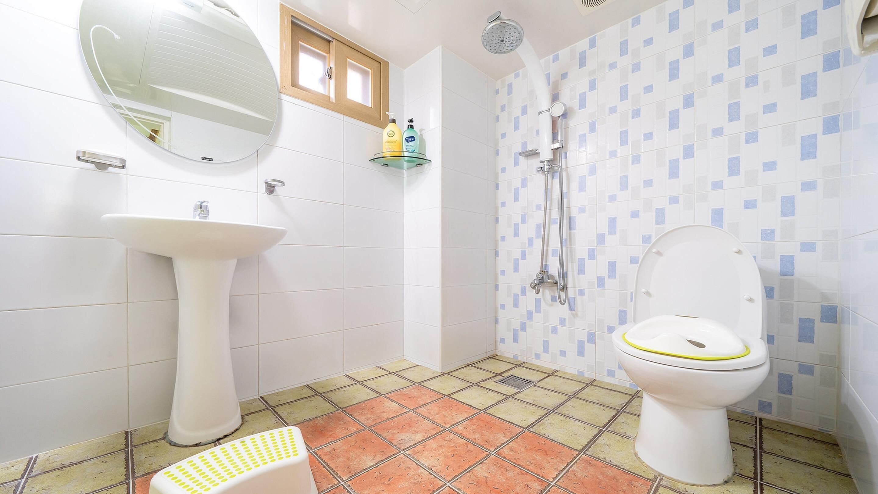 A bathroom with a pedestal sink, a toilet, a shower, and a small window.
