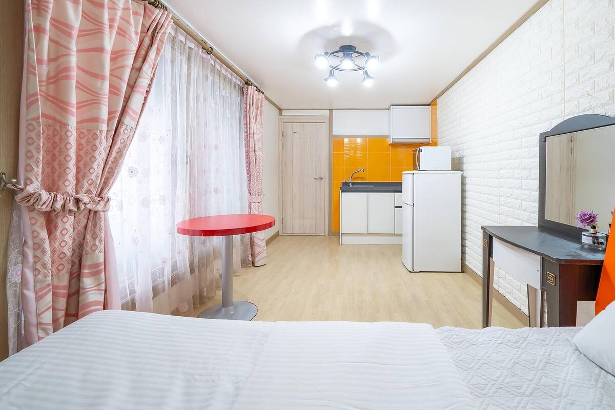 A hotel room with a bed, a small round table, a kitchenette, and a bathroom visible in the background.