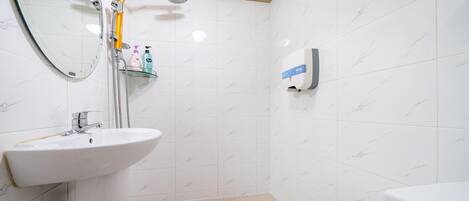 Baño con lavamanos blanco, espejo, ducha e inodoro.
