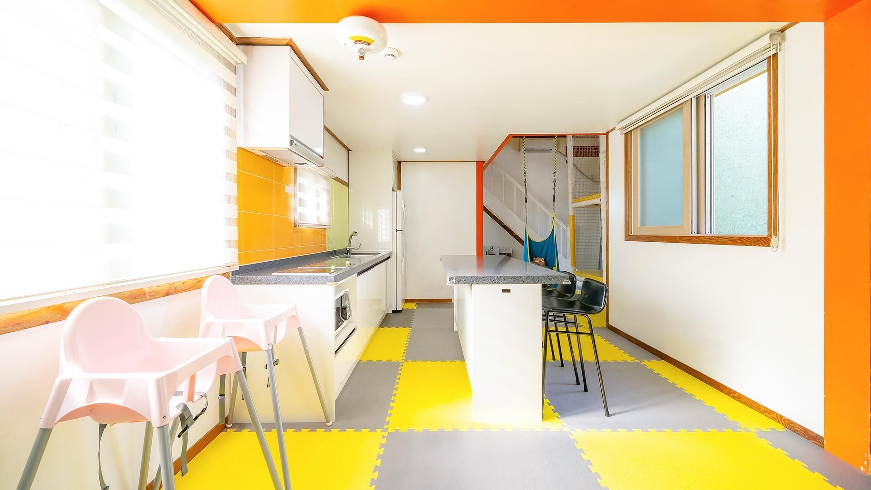A kitchen with a small island, two pink chairs, and a yellow and gray floor mat.