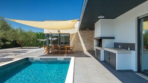 Un'area piscina moderna all'aperto con un set da pranzo e una stazione barbecue.