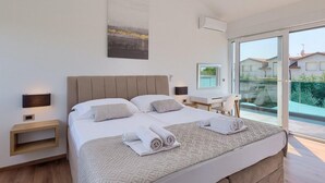 Camera moderna con un letto grande, comodini, una scrivania e vista su una piscina attraverso una porta in vetro.
