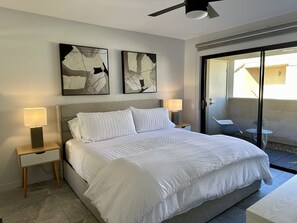 Ein modernes Hotelzimmer mit einem großen Bett, zwei Nachttischlampen, abstrakter Kunst an der Wand und einer Glastür zum Balkon.