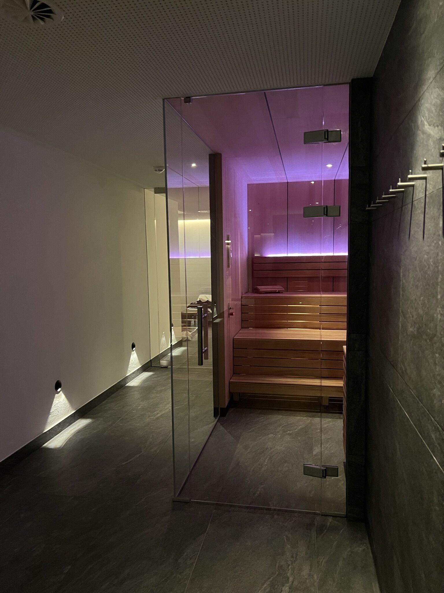 Ein modernes Interieur mit einer Glastrennwand, einer Holzbank und einer violett beleuchteten Wand.