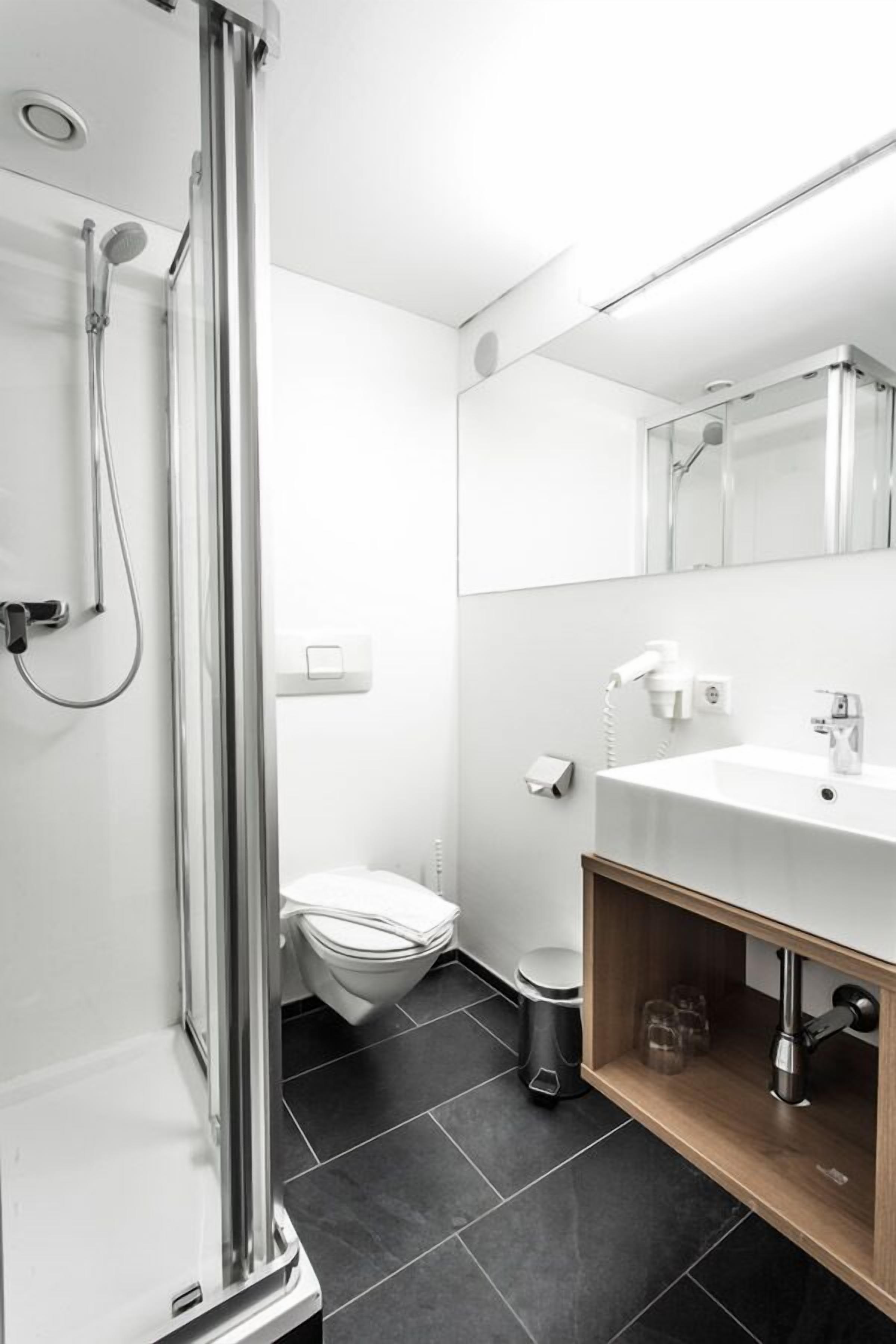 Un baño moderno con cabina de ducha de vidrio, un lavamanos blanco y un inodoro.