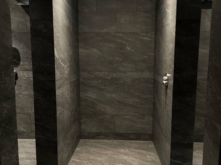A modern bathroom with dark stone walls and floor, recessed ceiling lighting, and a visible shower control panel.