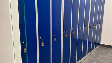 A row of blue lockers with metal handles and keychains, lined against a white wall in a hallway.