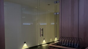 A modern sauna with glass walls, a wooden bench, and a heated floor.