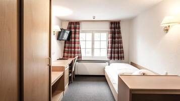 Een kleine hotelkamer met een bed, een bureau, een stoel, een televisie en een raam met gordijnen.