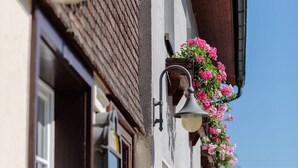 A building with a traditional facade, a window with a wooden shutter, and a flower box with pink flowers.