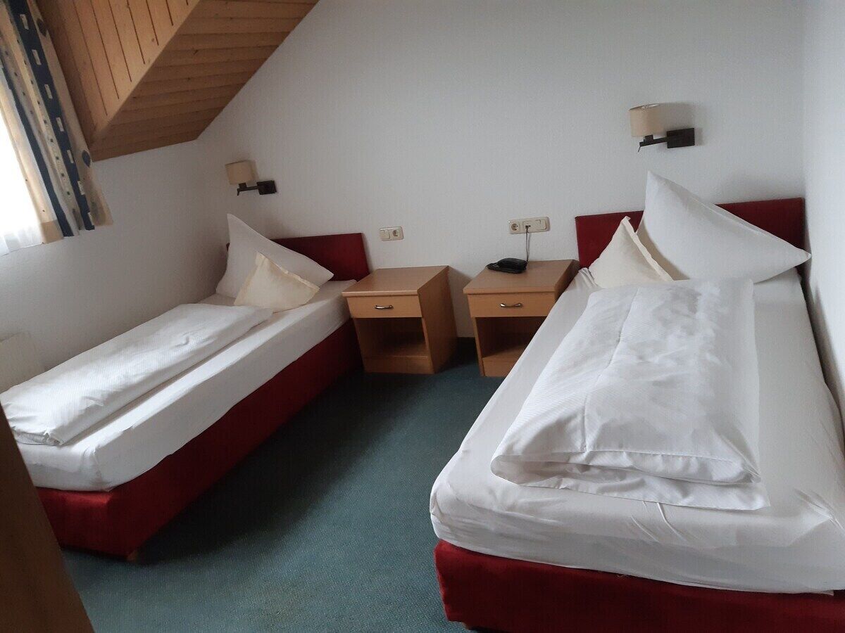A room with two single beds, a wooden nightstand, a desk, and a lamp.