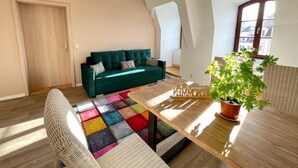 Ein modernes Wohnzimmer mit einem grünen Sofa, einem bunten Teppich, einem Holztisch und einer Topfpflanze.