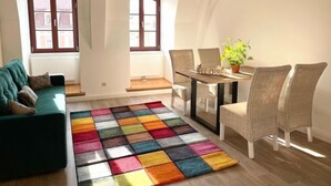 Ein geräumiges Wohnzimmer mit einem farbenfrohen Teppich, einem grünen Sofa und einem Essbereich mit Korbstühlen.