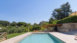 Ein rechteckiger Swimmingpool mit einer Steindeck und einer Pergola, umgeben von Grünpflanzen.