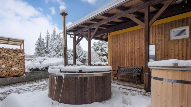 A wooden cabin with a hot tub and a bench, surrounded by snow-covered trees. - Pod Liščím kopcem 4+4 by Interhome (Dolni Branna)