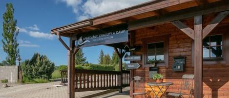 A wooden cabin with a sign indicating 'Apartment, Chalupy A Camp Pod Licem Kopcem'. There are outdoor tables and chairs, and a sign pointing to 'Camp' and 'Mobili Domy'.