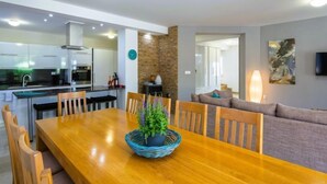 Una cocina moderna con armarios blancos y electrodomésticos de acero inoxidable, un comedor con mesa y sillas de madera, y una sala de estar con sofá y televisor de pantalla plana.