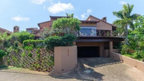 A modern house with a covered driveway, a stone wall, and lush greenery.