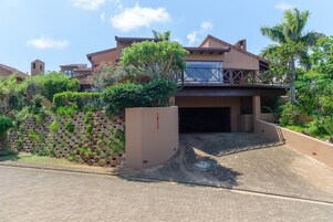 A modern house with a covered driveway, a stone wall, and lush greenery.