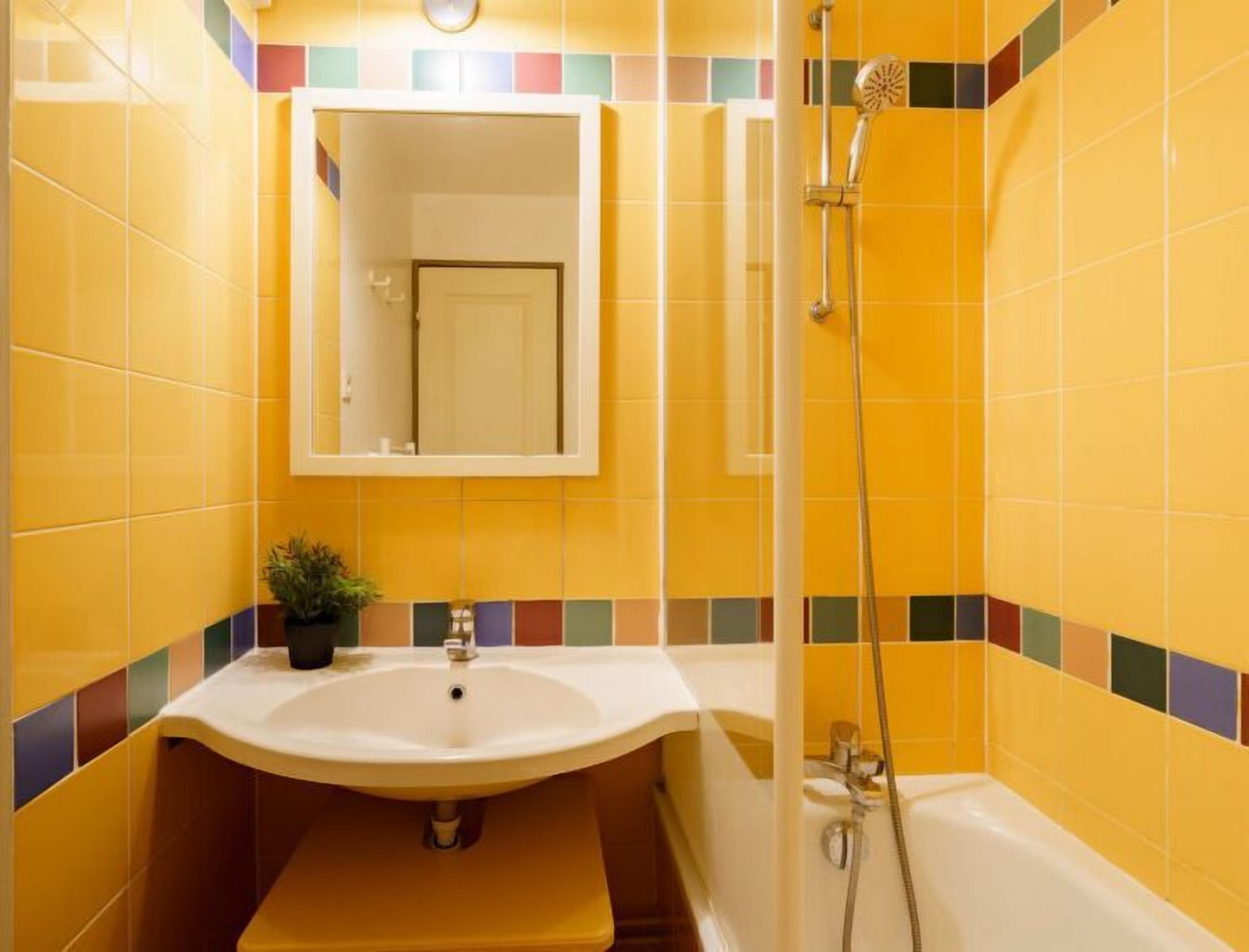 Une salle de bain avec des carreaux jaunes, un lavabo, un miroir et une douche.
