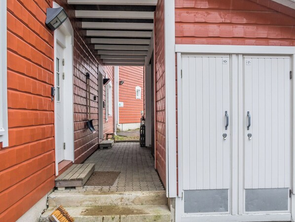 A covered outdoor area with a brick wall, a white door, and a small step leading to a porch.