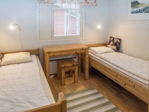 Et lille værelse med to senge, et træskrivebord med stol og et vindue med rullegardiner.