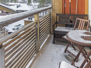 Ein Holzbalkon mit Metallgeländer, ein Holztisch mit einem Stuhl und eine Tür im Hintergrund.
