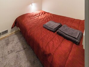 Un lit simple avec une couverture rouge et deux couvertures pliées.