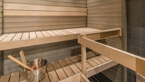 A sauna with wooden benches and a metal bucket with a brush.