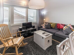 Un salon comprenant un téléviseur, un canapé, une chaise en bois et un meuble de rangement blanc.