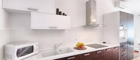 A modern kitchen with white cabinets, a stainless steel range hood, a microwave, and a sink with a fruit bowl.