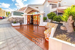 Welcome to our hotel, featuring a modern entrance with a glass door and stone walls, surrounded by outdoor seating areas and a small garden.