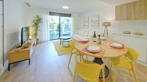 Un salon moderne avec un coin repas, comprenant une table ronde entourée de chaises jaunes, un canapé et un téléviseur posé sur un meuble.