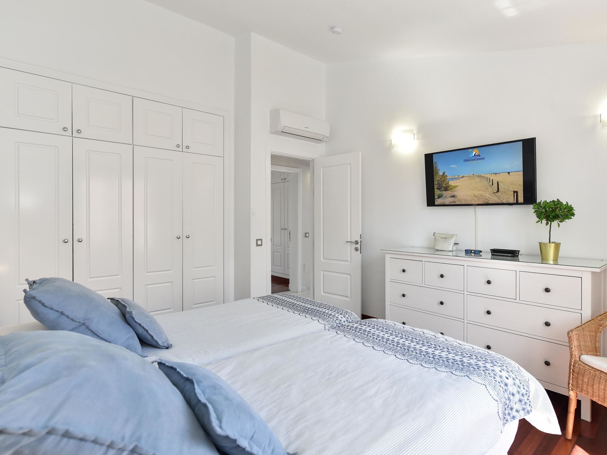 Un dormitorio con una cama grande, un aparador, un televisor y una puerta que da a otra habitación.