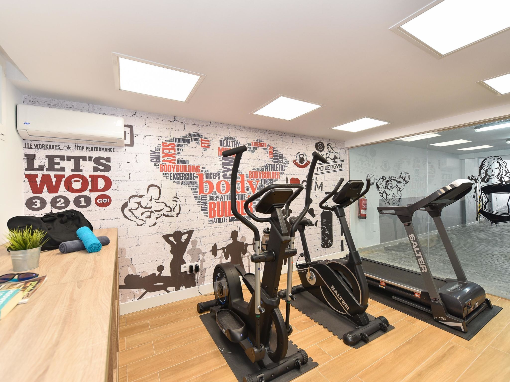Ein Fitnessraum mit Trainingsgeräten, einer motivierenden Wand und einem Holztisch mit Pflanze.