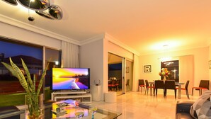A modern living room with a flat-screen TV, a glass coffee table, and a dining area with chairs and a table. - Meloneras Hills 19 by Interhome (Maspalomas)