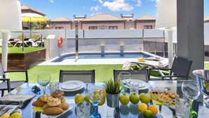 A dining table set with food and drinks, overlooking a swimming pool and a view of houses. - Meloneras Hills 19 by Interhome (Maspalomas)
