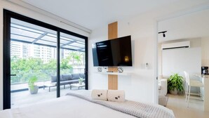 A modern bedroom with a large bed, a flat-screen TV mounted on a wooden panel, a balcony with outdoor seating, and a dining area with a table and chairs. - w* | Glorious 1BR w/ Terrace in San Francisco (Panamá)