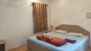 Una cama individual con cabecera, una ventana con cortinas, una mesita de noche y un enchufe en la pared.