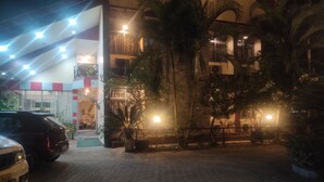 Un edificio con entrada pavimentada, palmeras y un automóvil estacionado.