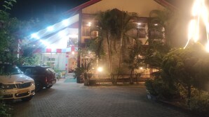 Un edificio con techo rojo y varios balcones, rodeado de vegetación y coches estacionados.