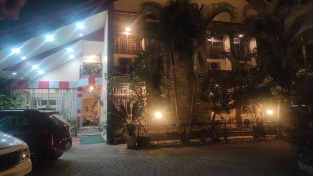 Un edificio de techo rojo con varios balcones, rodeado de palmeras y un área de acceso pavimentada.