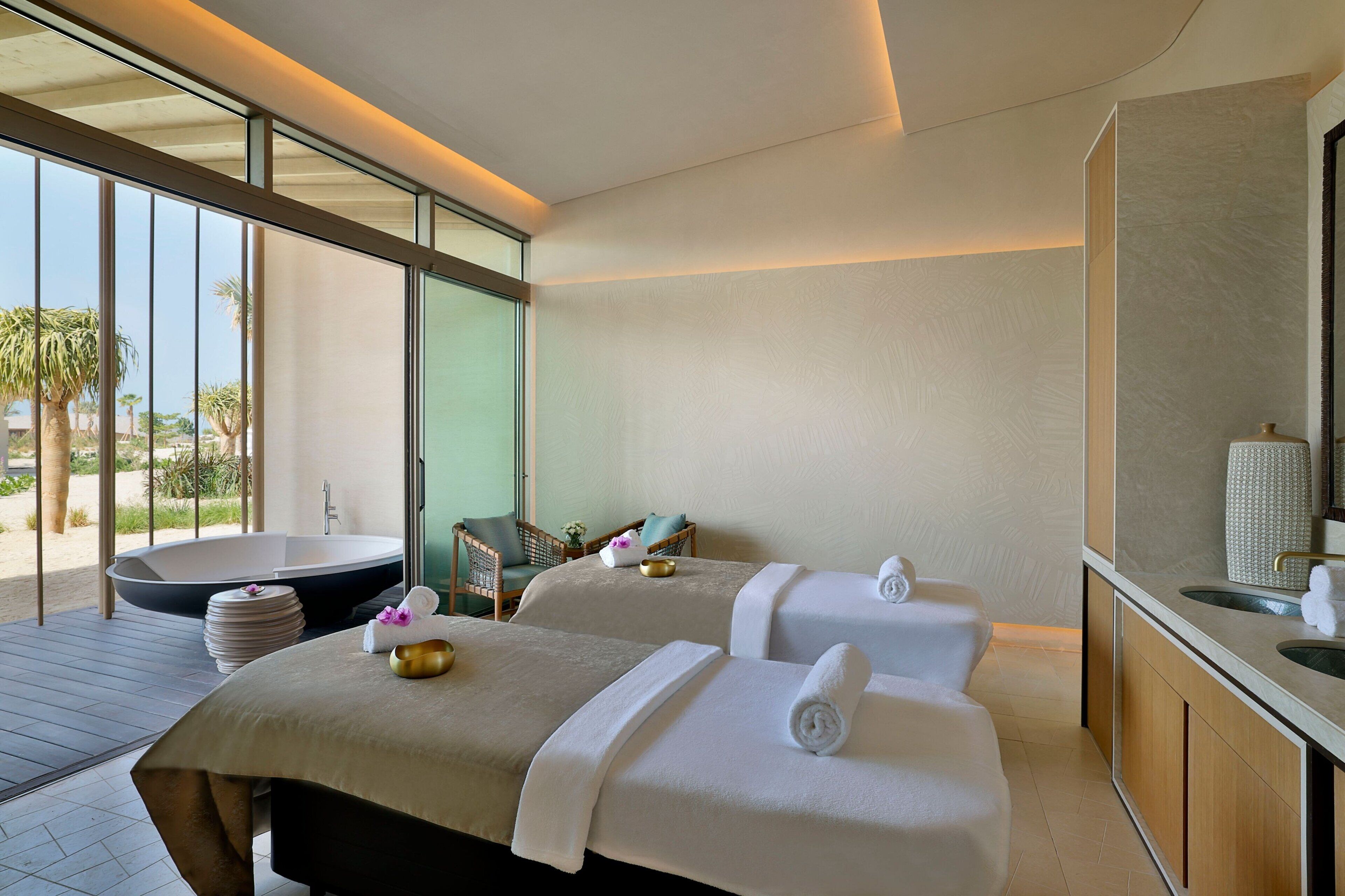A spa room with two massage beds, a large bathtub, and a wooden deck.